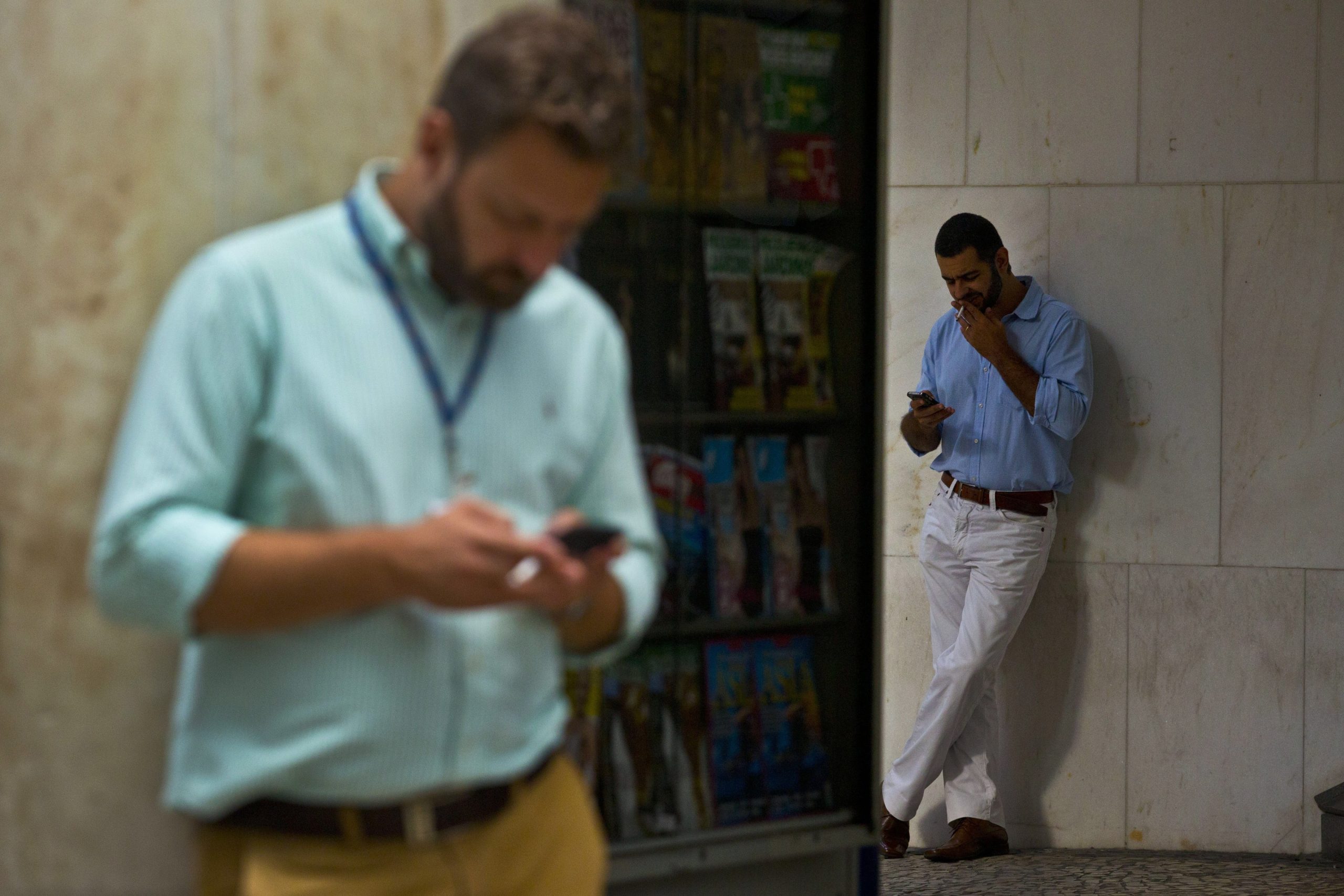A man smoking and another man on his phone