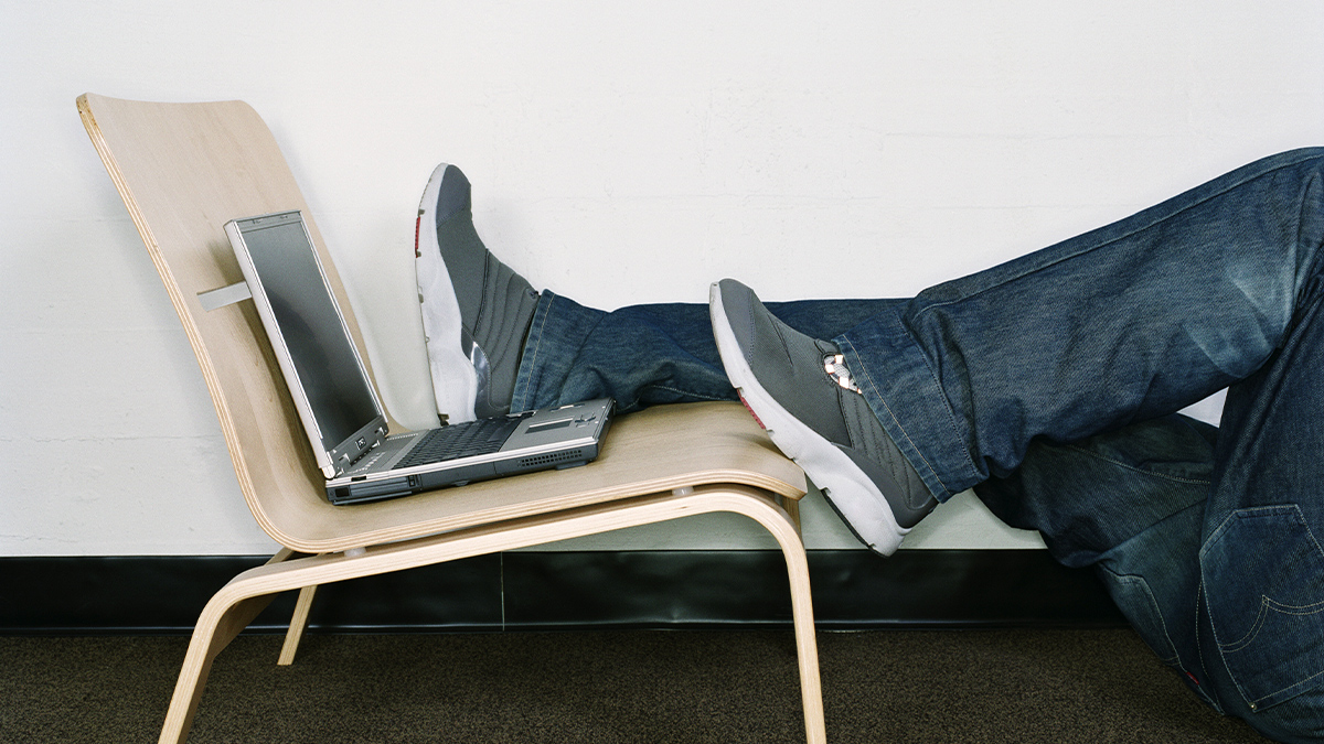 A man with his feet on a chair beside a laptop