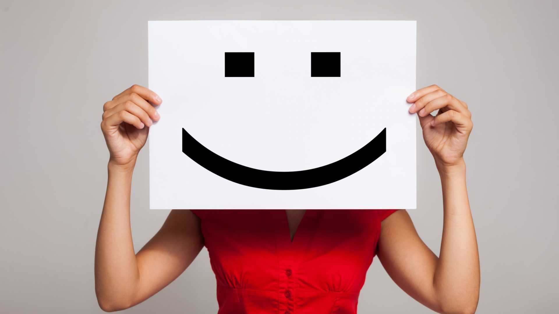 A woman holding a smiley face image in front of her face